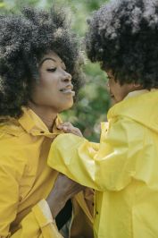 Mother and child sharing a tender moment in matching yellow raincoats amidst lush greenery.